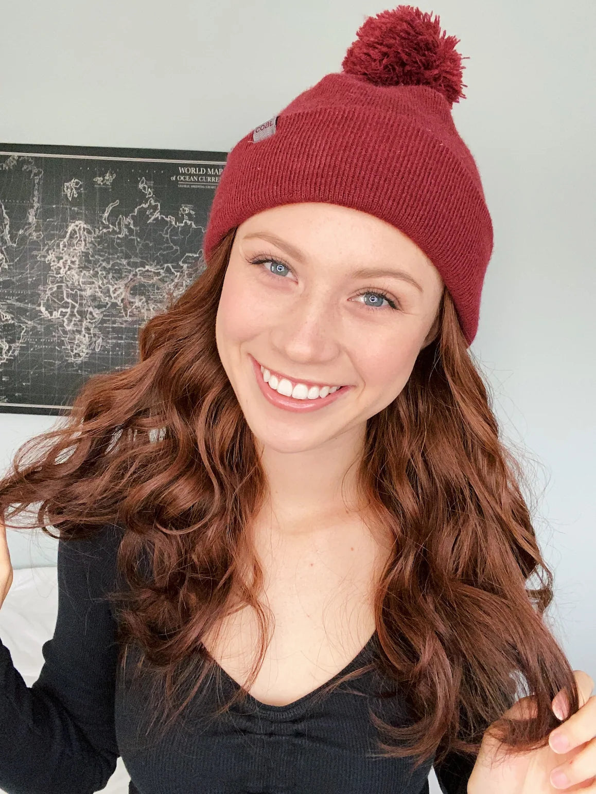 Woman wearing a red beanie with a pom-pom, smiling in front of a world map.