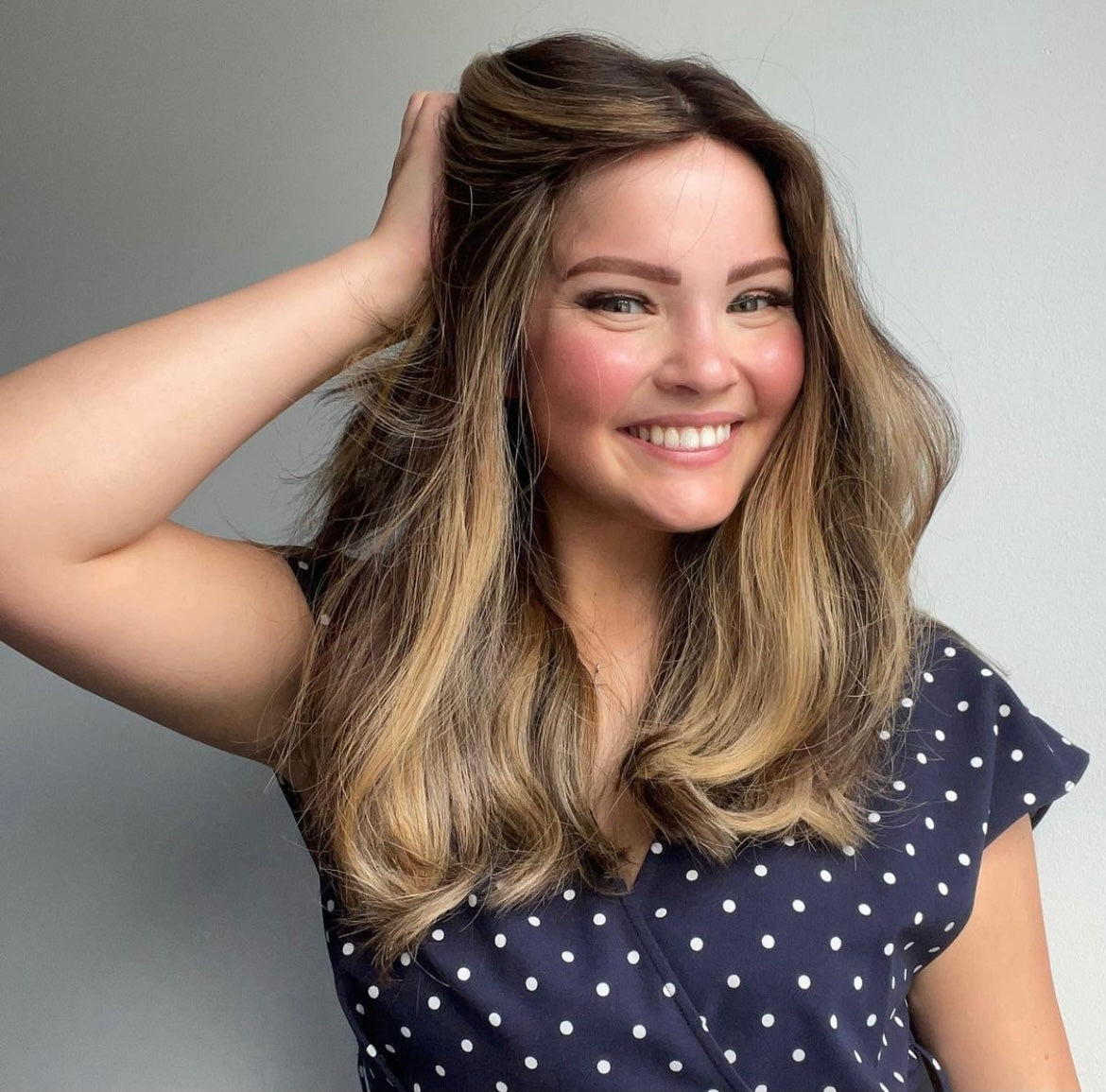 Woman with long, wavy hair smiling against a gray background